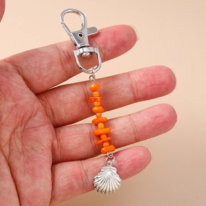 Detail of a silver seashell pendant keychain with orange stone beads held in hand