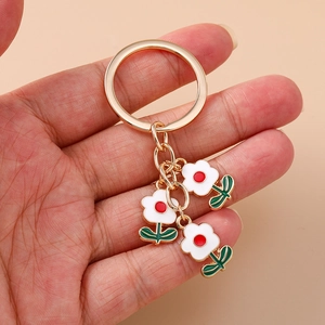 Porte-clés chic en alliage doré avec trois pendentifs en émail blanc en forme de fleurs