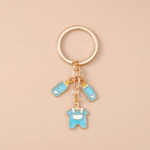 Detail of golden keychain with blue baby bottle charms and heart patterns on light background