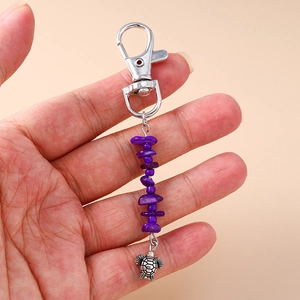 Detail of silver turtle keychain with purple natural stone beads held in hand
