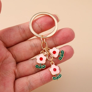 Gros plan détaillé du porte-clés doré avec trois fleurs en émail rose tenu en main