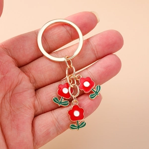 Porte-clés tendance avec pendentifs fleurs rouges et anneau doré tenu dans la main