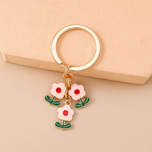 Détail d'un porte-clés fleur doré avec pétales en émail rose sur support beige chic