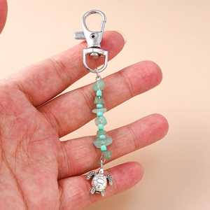 Detail of a sea turtle keychain with blue beads and green gravel stones held by hand