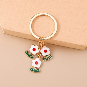Détail d'un porte-clés floral doré avec des pétales blancs et des feuilles vertes