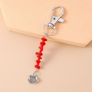 Detail of fish charm keychain with red stones and silver lobster clasp on beige stand