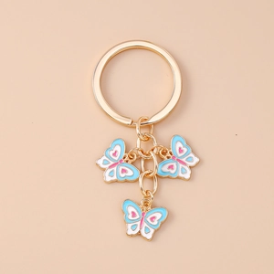 Dettaglio del portachiavi dorato con ciondoli a farfalla smaltati in blu, rosa e bianco