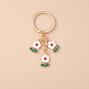 Vue détaillée d'un porte-clés doré avec trois fleurs en émail blanc et des pistils rouges