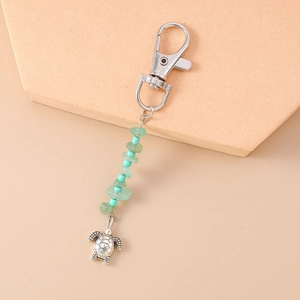 Detail of silver turtle keychain with turquoise beads on a warm geometric background