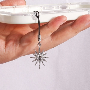 Elegant rhinestone sunburst star phone charm pendant hanging from a clear phone case