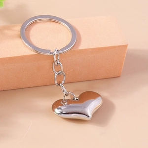 Close-up of polished silver heart-shaped keychain on a peach-colored minimalist background