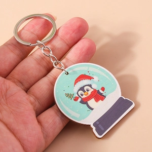 Gros plan d'un porte-clés de Noël en bois avec pingouin et boule de neige en main