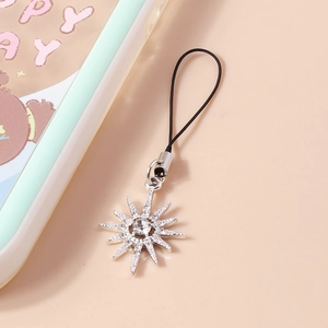 Detailed close-up of a silver sunburst phone charm with sparkling rhinestones and a black cord