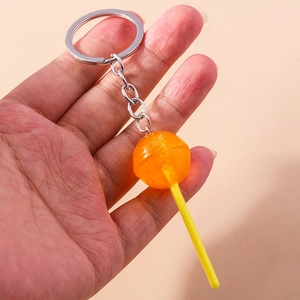 Detail of hand holding a creative orange lollipop keychain with gold glitter and silver ring