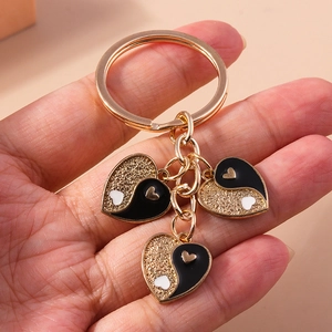 Détail de porte-clés cœur doré avec breloques Yin Yang en émail noir et paillettes dorées