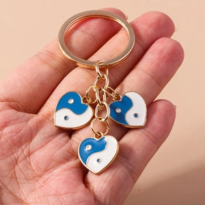 Détail d'un porte-clés doré avec trois breloques cœur Yin Yang bleu et blanc à la main
