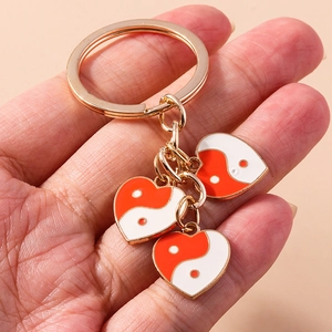 Détail d'un porte-clés cœur doré avec des breloques émaillées yin-yang orange et blanches