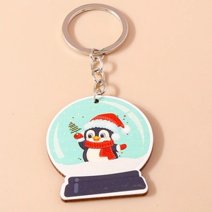 Détail d'un porte-clés de Noël avec motif de pingouin et boule à neige sur fond beige