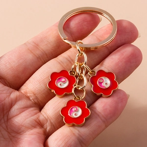Détail d'un porte-clés en métal doré avec fleurs rouges et motifs Yin Yang en émail