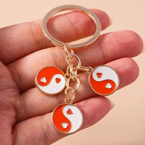Porte-clés doré tenu à la main avec trois breloques Yin Yang en forme de cœur rouge et blanc