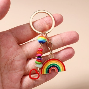 Rainbow enamel keychain with gold ring, heart charm and colorful beads held in hand