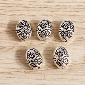Primer plano de cinco cuentas metálicas ovaladas plateadas con motivos florales en relieve