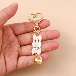 Portachiavi con cuore dorato fiocchi bianchi e perle tenuto in mano su sfondo rosa
