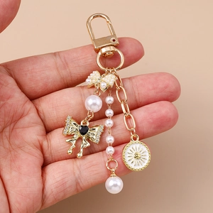 Golden keychain with pearl bow, rhinestone heart, and sun pendant held against a beige background