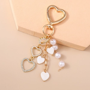 Detail of a gold heart keychain with pearls and rhinestones on a pink tray