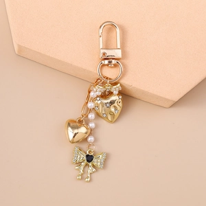 Close-up of golden heart keychain with white pearls, rhinestones and a black bow detail