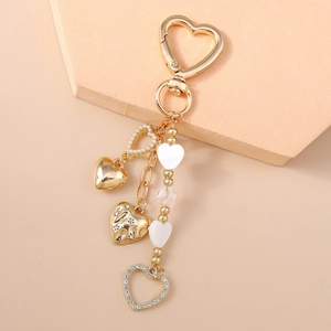 Detail of a gold heart keychain with pearls, rhinestones, and enamel charms on a display stand
