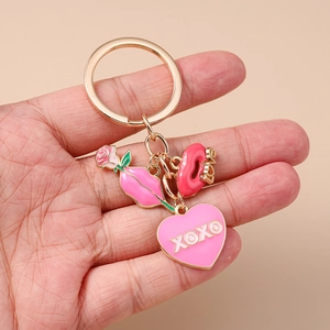 Détail d'un porte-clés doré avec cœur XOXO, rose et lèvres, tenu dans la main