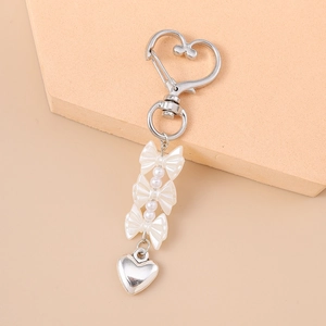 Dettaglio della chiusura a cuore argento e portachiavi con perle su fondo beige caldo