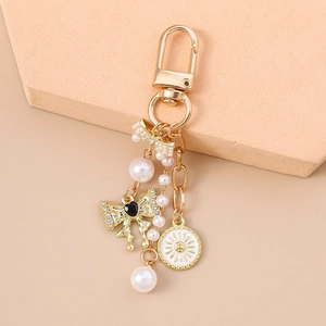Golden keychain with pearl bow, sun medallion and heart charm on beige geometric blocks