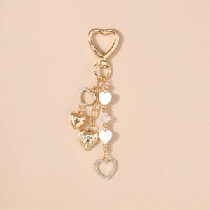 Golden heart keychain with white pearls and sparkling rhinestone crystal charms on beige background
