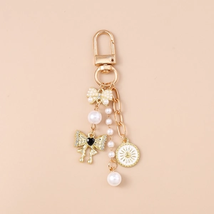 Detail of gold keychain with pearl bow, black heart charm and sun pattern pendant