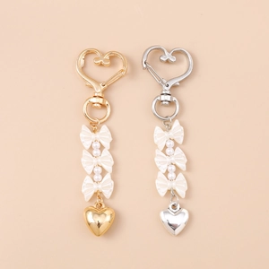 Eleganti portachiavi a cuore e fiocco in oro e argento con perle su sfondo neutro