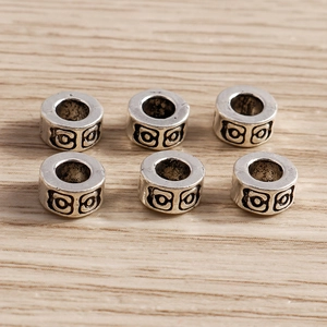 Vista macro de seis cuentas espaciadoras de plata antigua con patrones vintage en madera