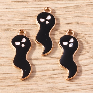 Detailed macro view of black enamel ghost charms with gold plating on light wood surface