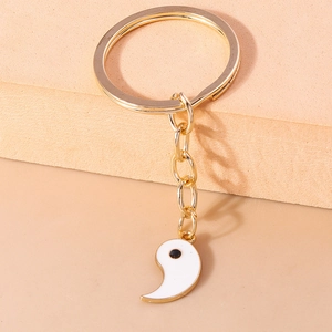Détail d'un porte-clés yin yang doré avec breloque demi-poisson en émail blanc pur