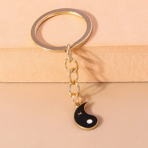 Détail d'un porte-clés yin yang doré avec breloque cœur en émail noir sur supports
