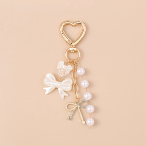 Detail of golden heart keychain featuring white resin bows and elegant pearl charms