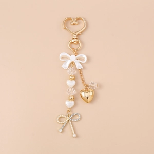 Detailed view of golden heart keychain with white bow, pearls and rhinestone bow charm