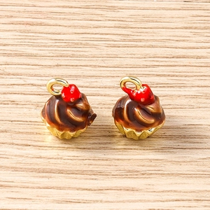 Macro detail of chocolate cupcake charm with brown enamel and red berry accent on gold base