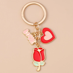 Détail d'un porte-clés doré avec rose rouge, cœur et breloques LOVE sur fond rose