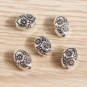 Detalle de cuentas metálicas ovales con grabado floral vintage para joyería y collares