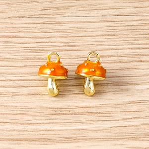 Macro view of handmade mushroom charms with orange enamel and gold metal hanging loop