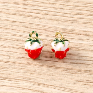 Macro shot of two strawberry pendants with red enamel and golden rings on wood background