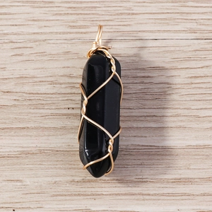 Detailed close-up of a black hexagonal stone pendant with gold wire wrap on wood
