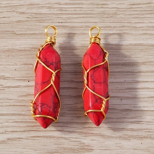 Macro shot of red hexagonal crystal pendants with golden wire wrap on wood background